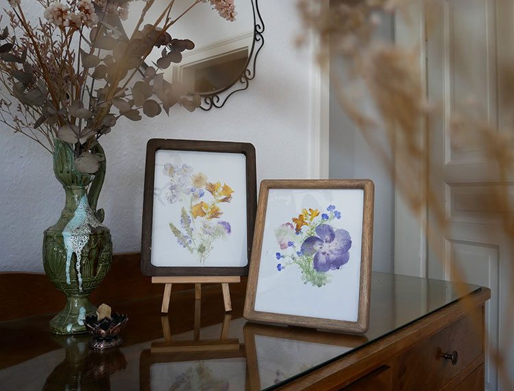 De zelfgemaakte bloemenafdruk is te zien in twee fotolijstjes op een ladekast.