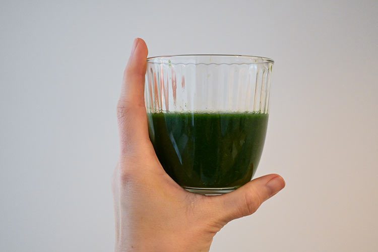 Eine Hand hält grüne Farbe in einem Wasserglas hoch.