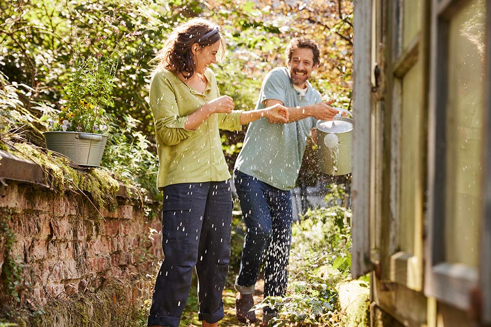 Mann und Frau spielen mit Wasser im Garten zur Abkühlung bei Hitze.