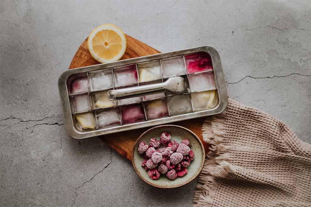 Selbst gemachte Eiswürfel mit Früchten liegen in einer Eiswürfelform auf einer Arbeitsplatte.