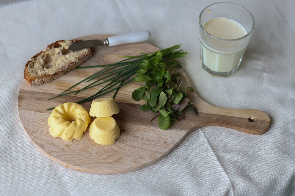 Selbst gemachte Butter liegt mit frischen Kräutern und einer Scheibe Brot auf einem Schneidebrett aus Holz.