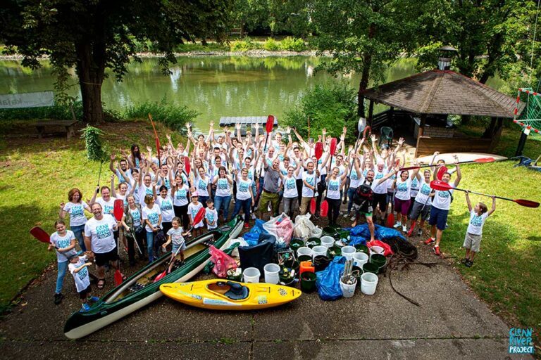 Eine Gruppe steht mit Ausrüstung für ein Clean-up vor einem Fluss.