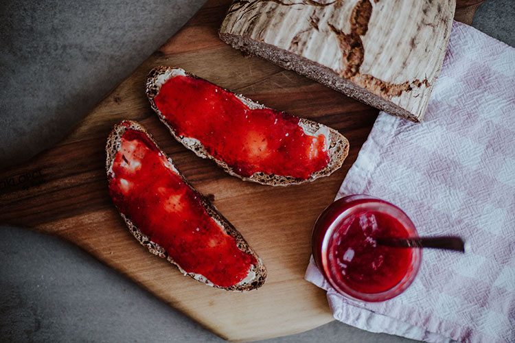 Frisch aufgeschnittenes Sauerteigbrot ist mit Erdbeermarmelade bestrichen.